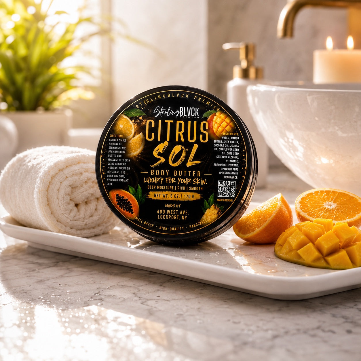 SterlingBLVCK Premium Citrus Sol Body Butter on a bathroom tray with towels, orange, and mango.