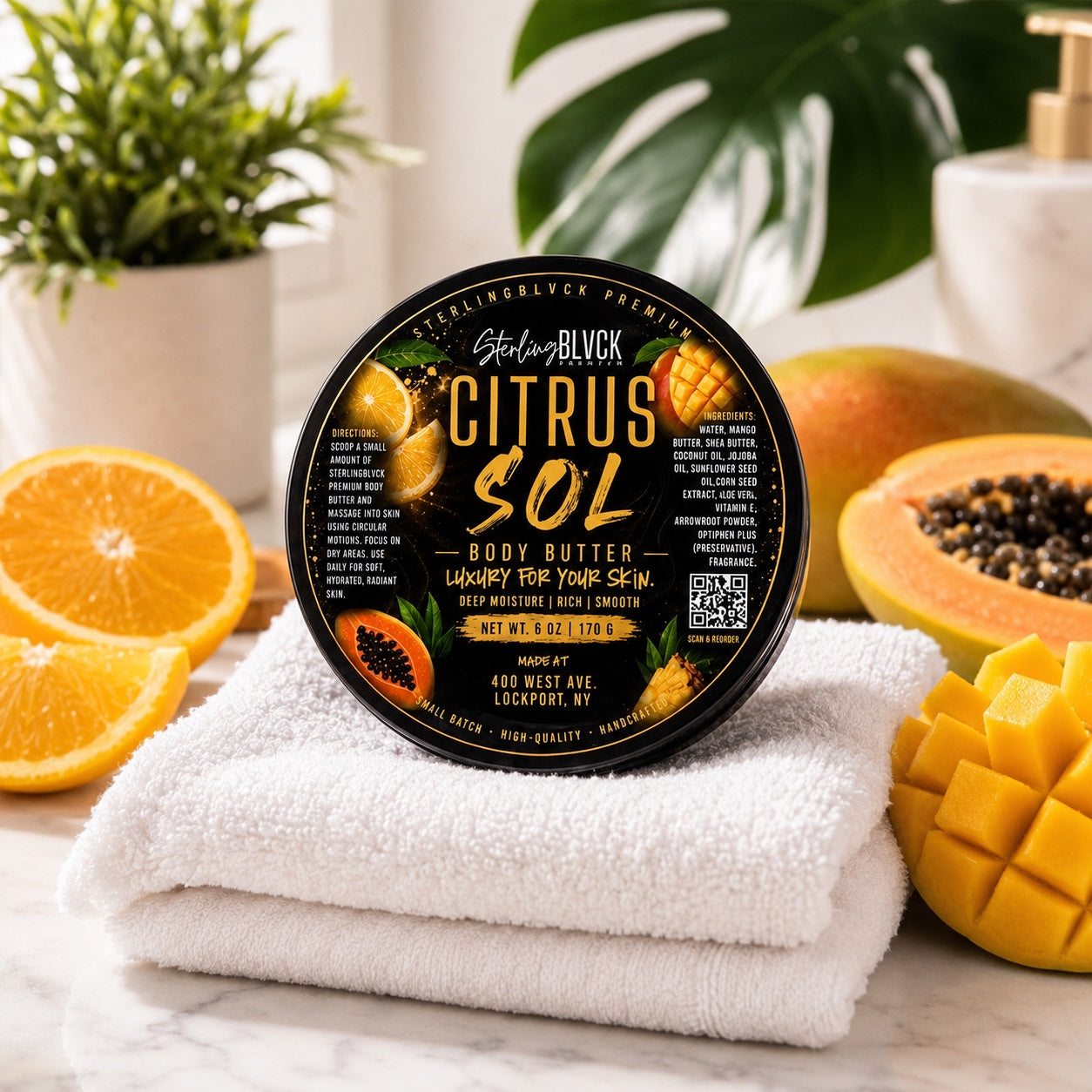 SterlingBLVCK Premium Citrus Sol Body Butter in a bright spa setting with white towels, orange, mango, and papaya.