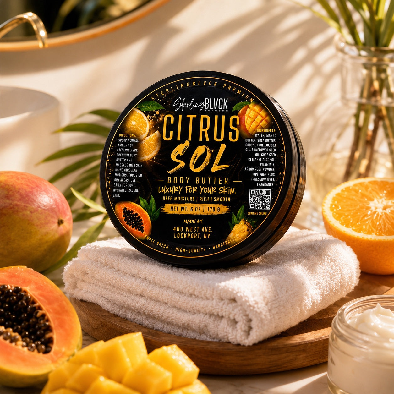 SterlingBLVCK Premium Citrus Sol Body Butter displayed on white towels with orange, mango, and papaya.